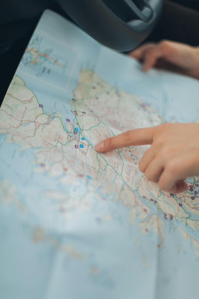 A woman's hand pointing at a location on a world map inside a car, highlighting navigation and travel planning.